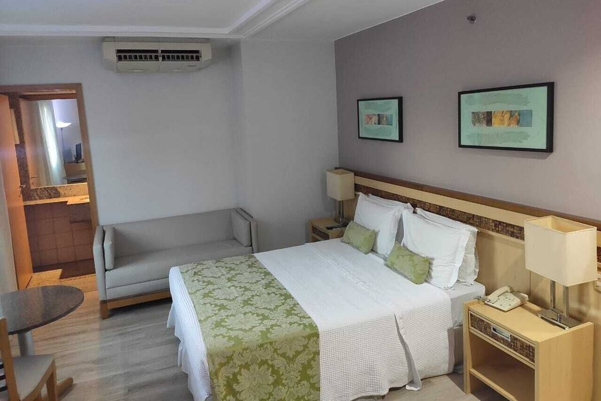A hotel room with a bed, bedside table, lamp, and a small table.