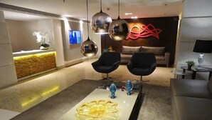 A modern living room with a central glass coffee table, two black armchairs, a sofa, and a decorative wall piece.