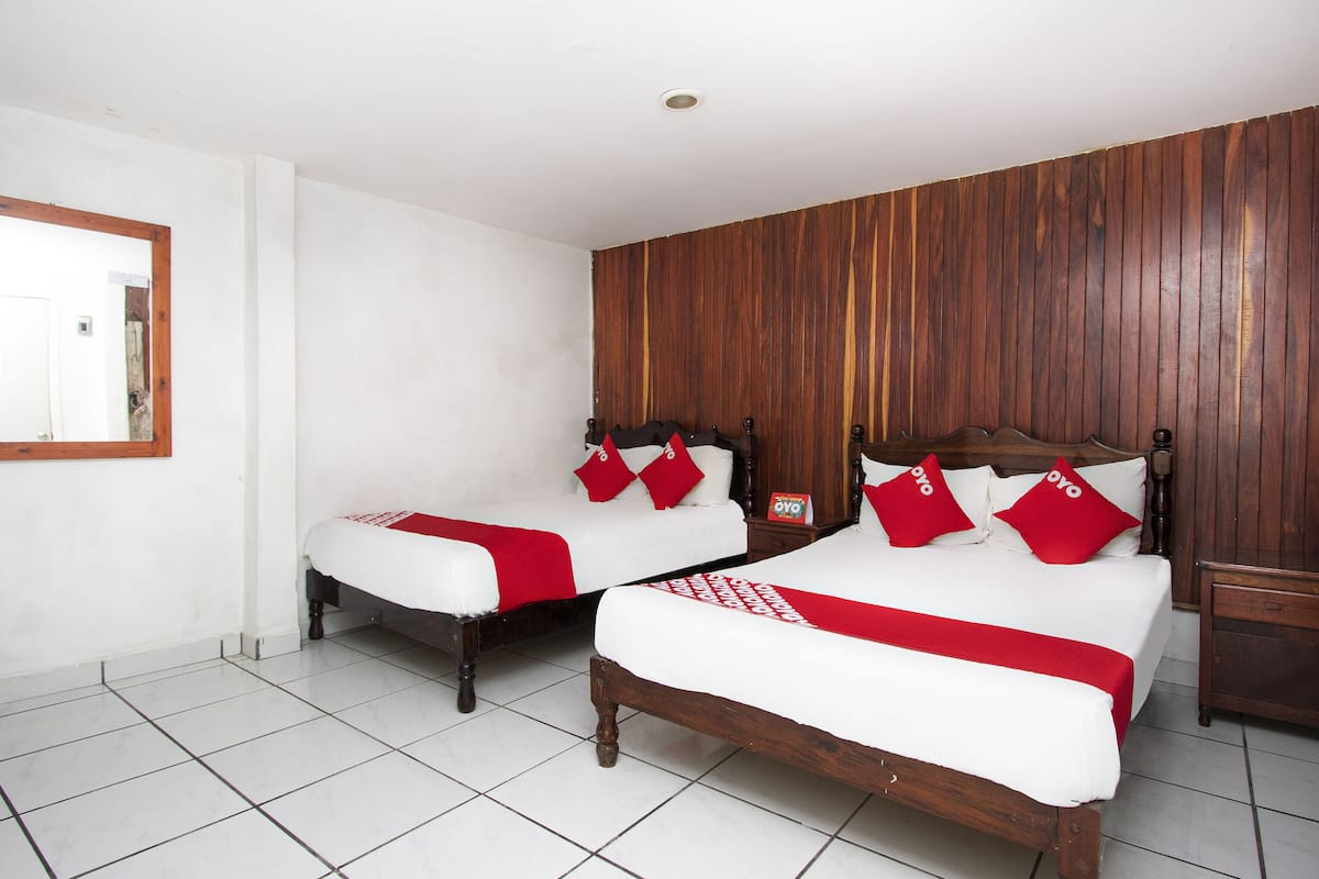 A hotel room with two beds, white bedding, red pillows, wooden headboards, and a tiled floor.