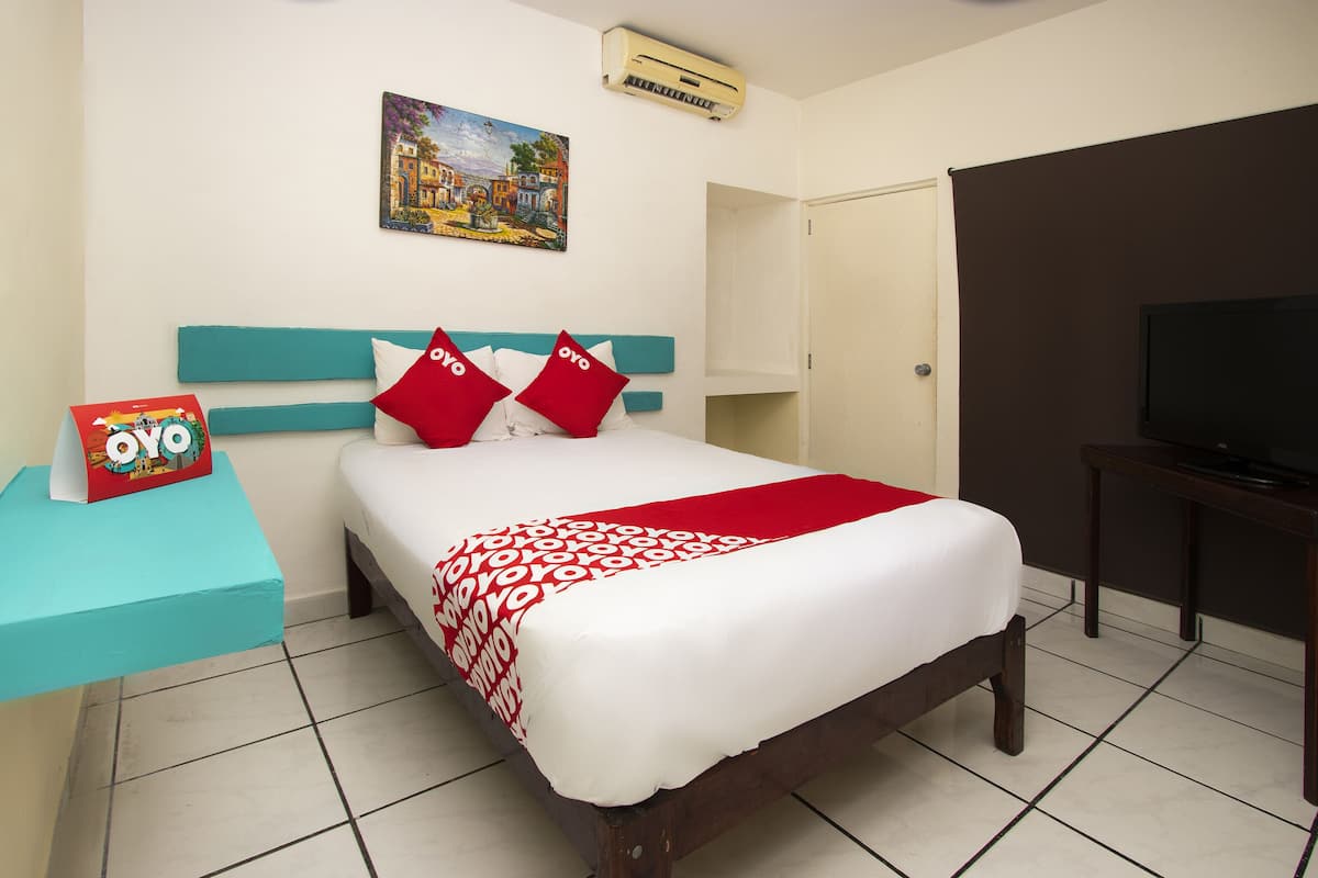 A hotel room with a bed, a TV, a painting on the wall, and a sign above the bed.