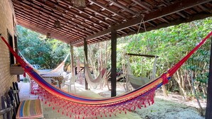 A covered outdoor area with a hammock, a bench, and a table. - Refúgio verde na praia de Pipa (Tibau do Sul)