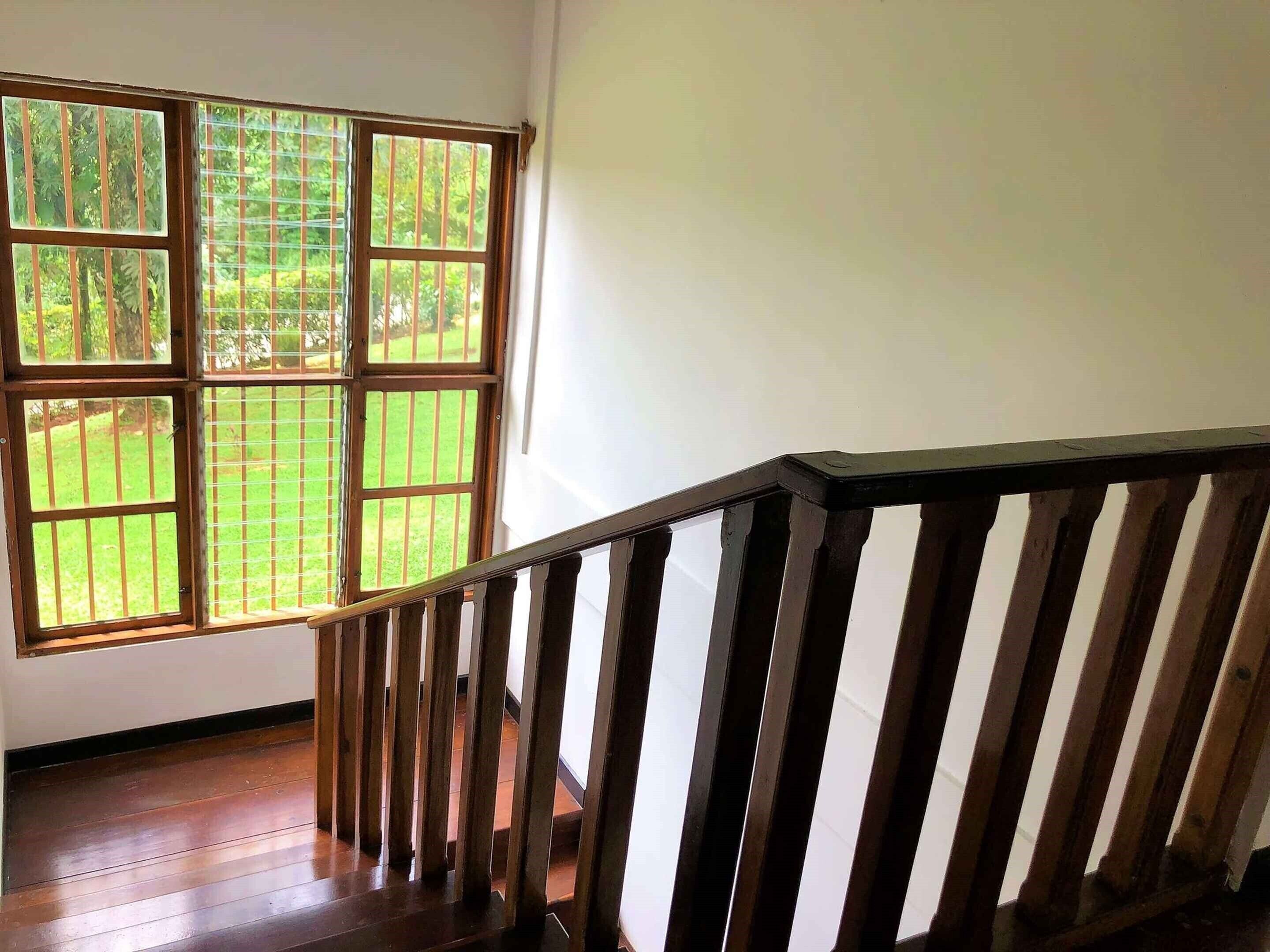 A wooden staircase with a railing leading to a room with a large window overlooking a grassy area.