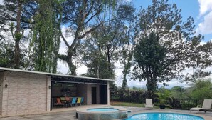 A swimming pool with a curved edge, surrounded by a patio area with chairs and a covered seating area. - Casa Naranjito (Naranjito)