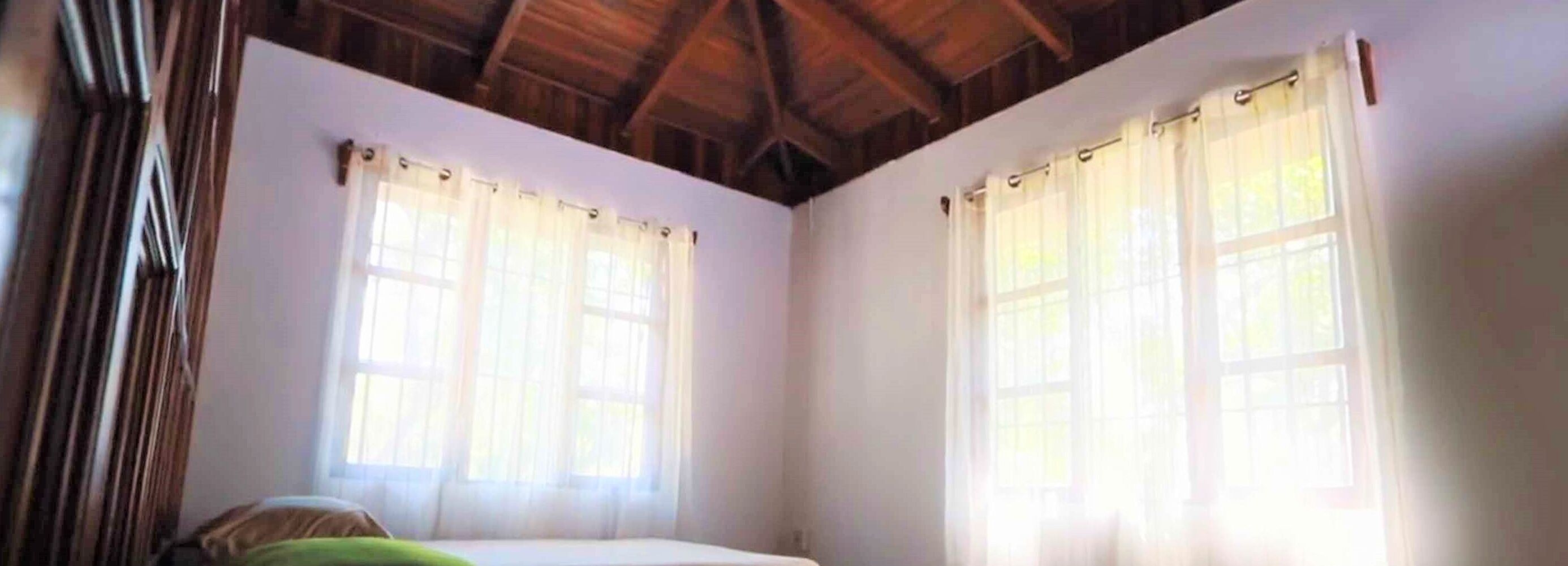 A room with two windows, wooden ceiling beams, and a bed.