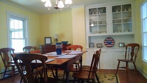 Une salle à manger avec une table et des chaises en bois, un lustre, une fenêtre et un buffet contenant de la vaisselle.