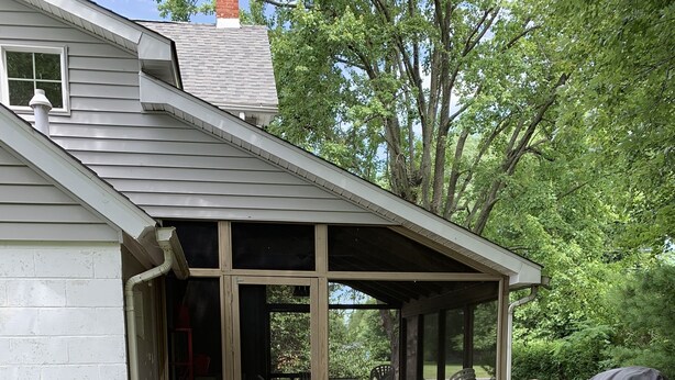 Une terrasse extérieure couverte, équipée d’un barbecue, de sièges et d’une plante en pot.