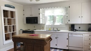 Une cuisine avec des meubles blancs, une table en bois, un four à micro-ondes, une machine à café et un lave-vaisselle.