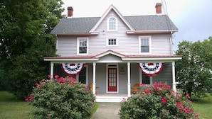 Une maison à deux étages avec un porche, une porte rouge et des décorations aux couleurs du drapeau américain.