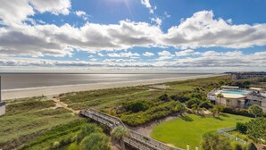 Een kustgezicht met een strand, een houten pier en een gebouw met een zwembad.