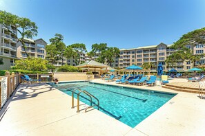 A swimming pool with lounge chairs and umbrellas, surrounded by multi-story buildings with balconies. - Family Villa | Ocean/Pool Views, Balcony, Bikes, Close to Shops/Dining (Hilton Head Island)