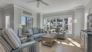 A spacious living room with a large window, a ceiling fan, and a sign reading "SEASIDE". - Family Villa | Ocean/Pool Views, Balcony, Bikes, Close to Shops/Dining (Hilton Head Island)