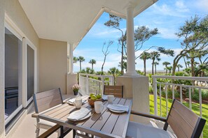 A balcony with a table set for two, chairs, a potted plant, and a view of palm trees and the ocean. - Family Villa | Ocean/Pool Views, Balcony, Bikes, Close to Shops/Dining (Hilton Head Island)