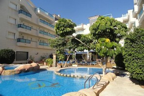En swimmingpool omgiven av en byggnad med balkonger, ett takförsett sittområde och frodig grönska.
