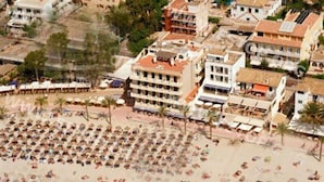 Vista aérea de una playa con filas de sillas de playa y sombrillas, rodeada de edificios con balcones.