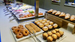 Un buffet proposant une variété de plats, notamment des pâtisseries, des beignets, ainsi qu’un assortiment de viandes et de fromages.