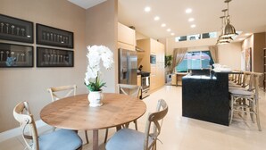 A modern kitchen with a central island, wooden dining table with chairs, and a potted orchid. - Near Disney, Family Friendly, Free Parking, Wi-Fi, Heated Pool (Kissimmee)