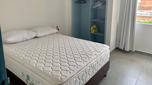 Cama bem arrumada com colchão estampado em quarto com guarda-roupa azul e janela com cortinas.