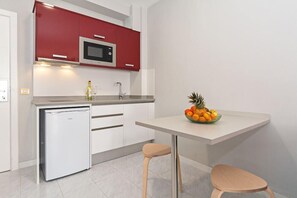 A compact kitchen with white cabinets, a red microwave, a small fridge, and a fruit bowl on the counter. - Oceano Apartments - Adults Only (Teguise)