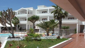Un patio de hotel con piscina, palmeras y un edificio blanco con balcones.