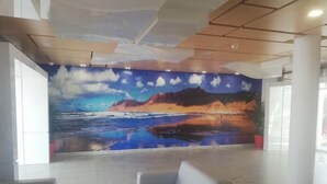Un vestíbulo con un mural de una playa, un sofá gris y una mesa de centro blanca.