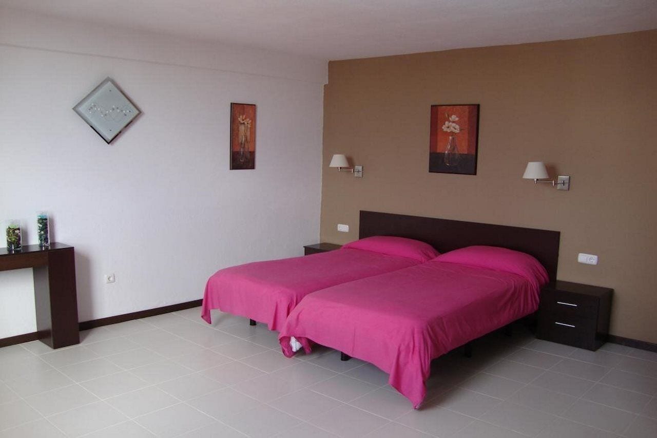 Un dormitorio con dos camas, una mesita de noche, un escritorio y dos lámparas de pared.