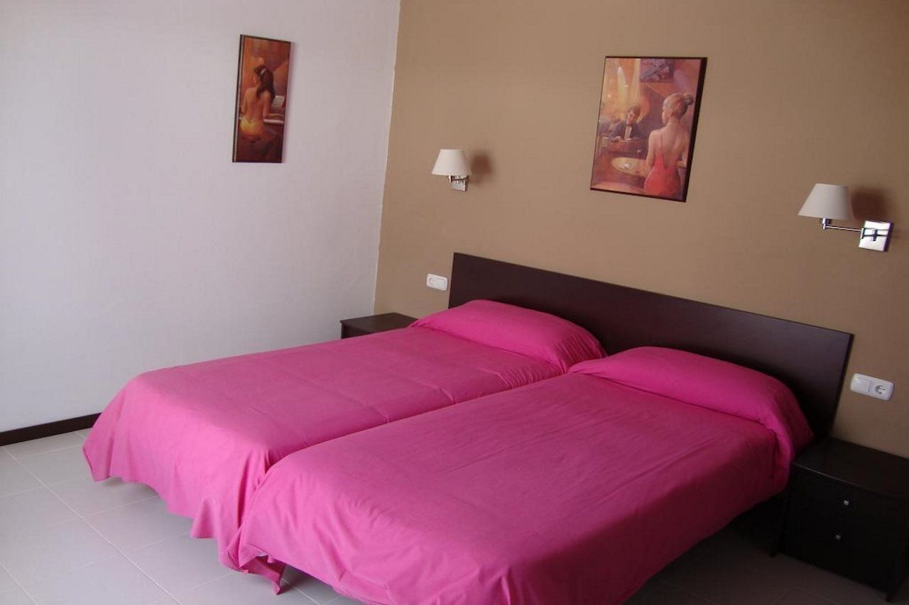 Een kamer met twee bedden, elk met een roze sprei, een donker hoofdbord en twee nachtkastjes met lampen.