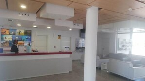 Un espace d’accueil comprenant un comptoir de réception blanc, une grande colonne blanche et un coin salon avec un canapé et des fauteuils blancs.