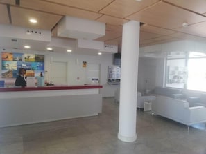 A reception area with a white reception desk, a large white pillar, and a seating area with a white sofa and armchairs. - Oceano Apartments - Adults Only (Teguise)