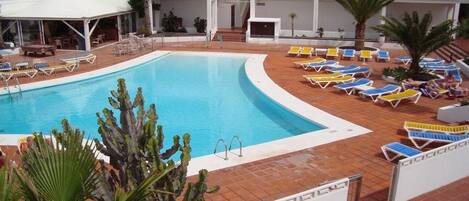 A pool area with lounge chairs and a white building in the background.