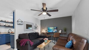 A modern living room with a sofa, a coffee table, a TV, and a ceiling fan. - 》Hip Urban Getaway Next to Downtown, with Firepit, 3 Bedrooms, Sleeps 6《 (TAMPA)