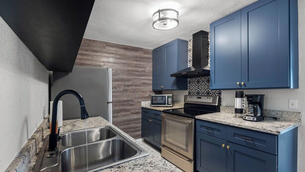 A modern kitchen with a stainless steel sink, a microwave, a stove, and blue cabinets. - 》Hip Urban Getaway Next to Downtown, with Firepit, 3 Bedrooms, Sleeps 6《 (TAMPA)