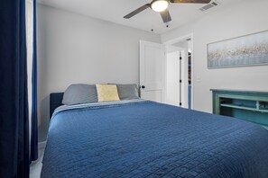 Une chambre à coucher comprenant un lit, un ventilateur de plafond, une porte et une œuvre d’art accrochée au mur.
