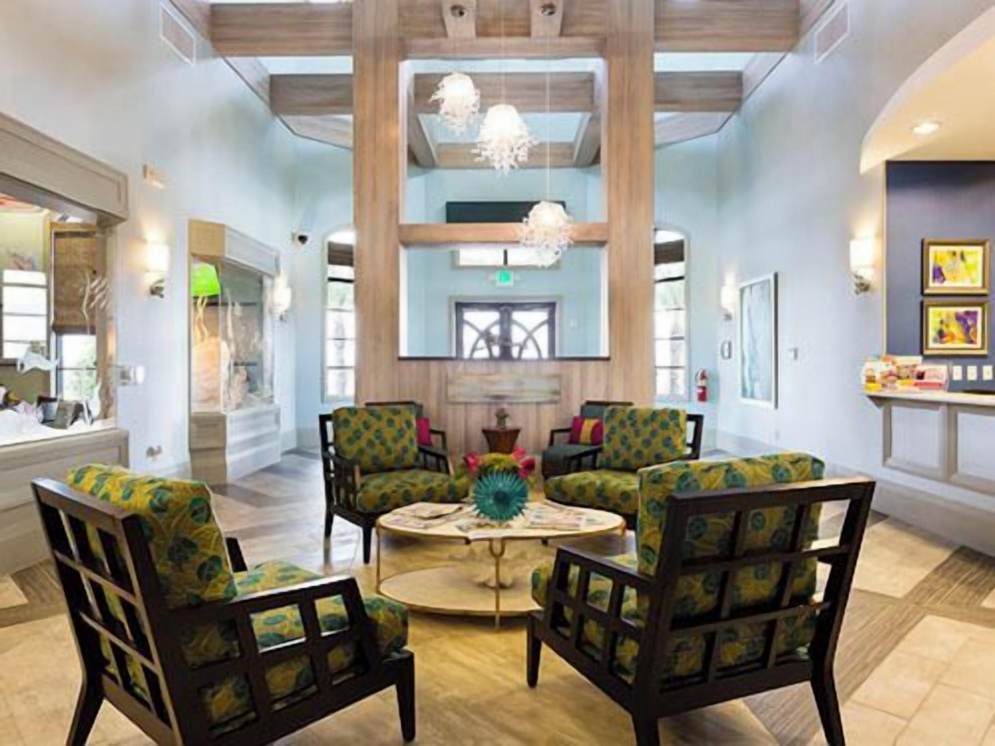 A lobby with a high ceiling, wooden beams, and a central chandelier. There are four armchairs with patterned upholstery and a round coffee table with decorative items.