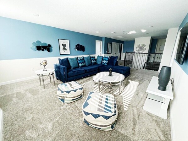 A living room with a blue sofa, two ottomans, a coffee table, and a white side table. - Luxury 7 Bedroom 5 bath pool Home 208 (Four Corners)