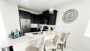 Une cuisine moderne avec des meubles de couleur sombre, un grand îlot central et un coin repas équipé de quatre chaises.