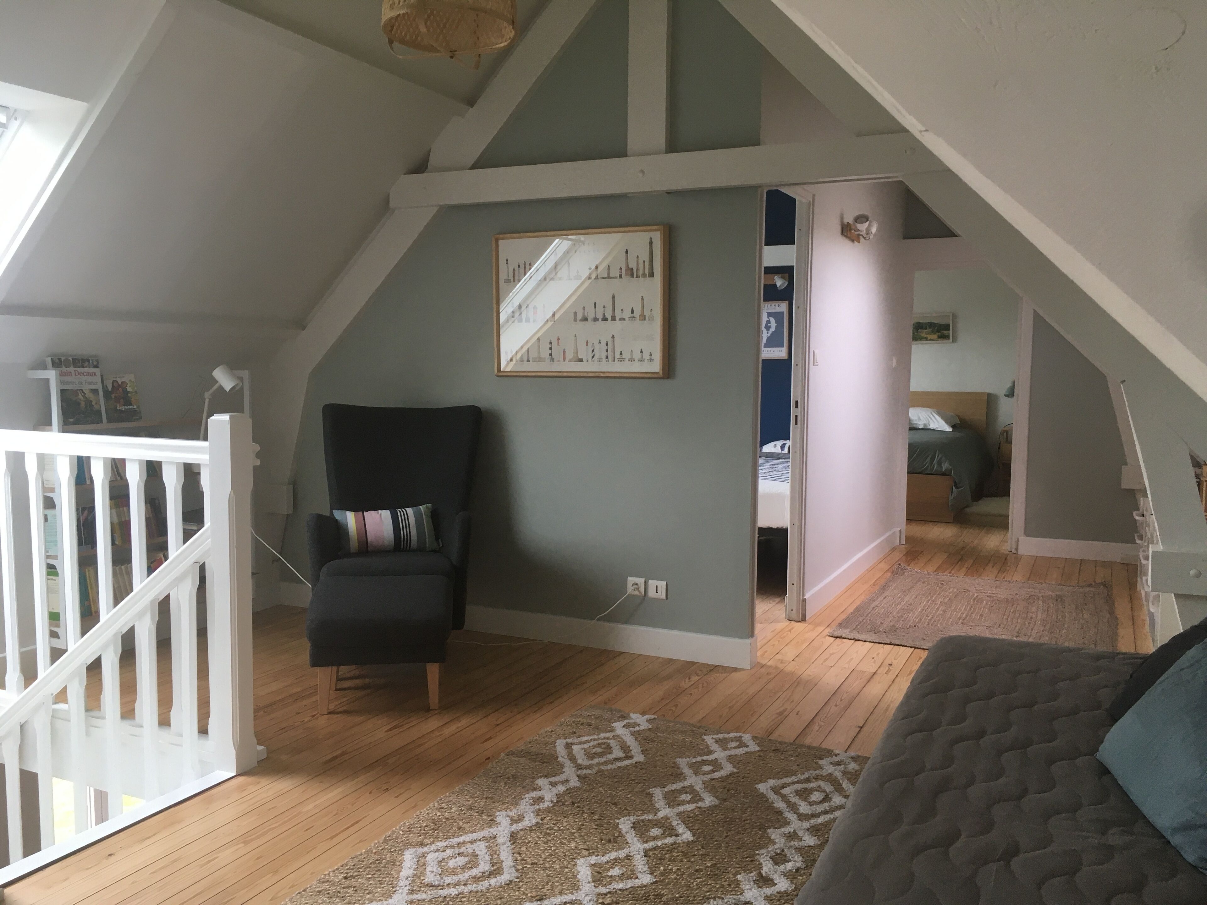 Ein Schlafzimmer im Loft-Stil mit schrägverdeckter Decke, einem schwarzen Sessel, einem gemusterten Teppich und einem Bett mit blauem Kissen.