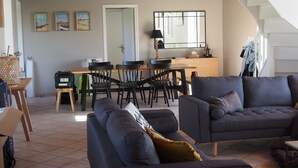 A modern living room with a sofa, a dining area with chairs, a kitchen, and a staircase.