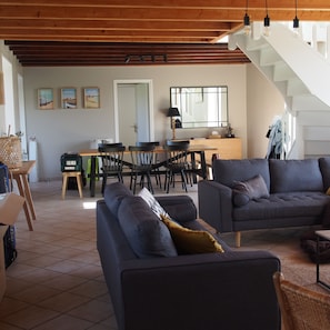 A modern living room with a sofa, a dining area with chairs, a kitchen, and a staircase.