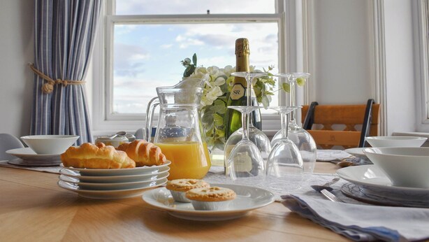 Ein Frühstückstisch mit Croissants, Orangensaft und Champagnergläsern an einem Fenster mit Vorhängen.
