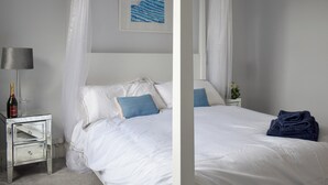 Ein Schlafzimmer mit Himmelbett, Nachttisch mit Flasche und Glas sowie einem gerahmten Bild an der Wand.