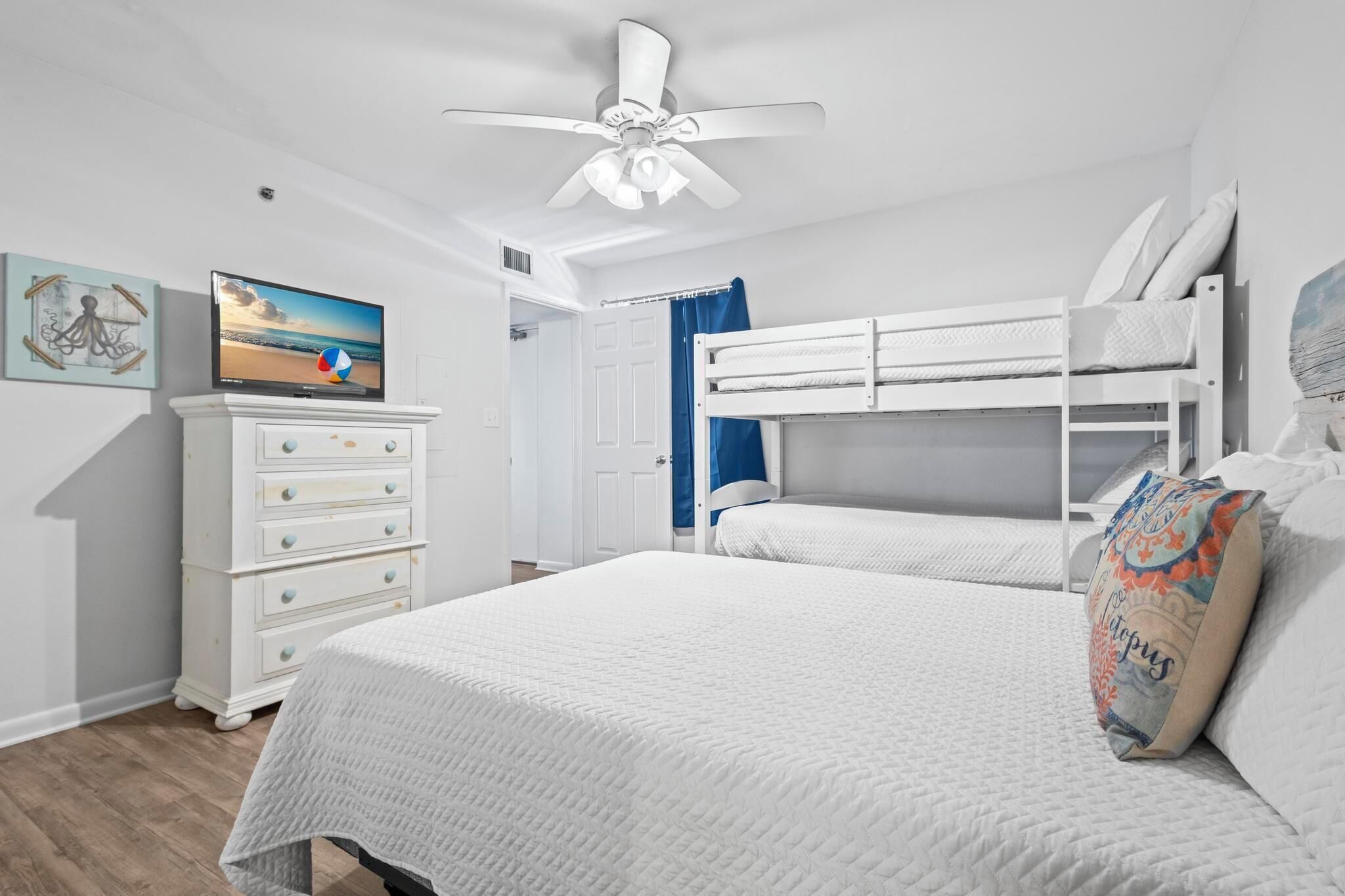 Une chambre avec un lit superposé, un téléviseur posé sur une commode et un ventilateur de plafond.