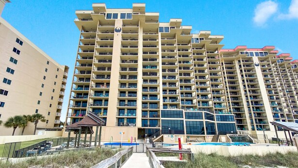 Un hotel alt amb nombrosos balcons, una piscina i un passeig que condueix a l'entrada.