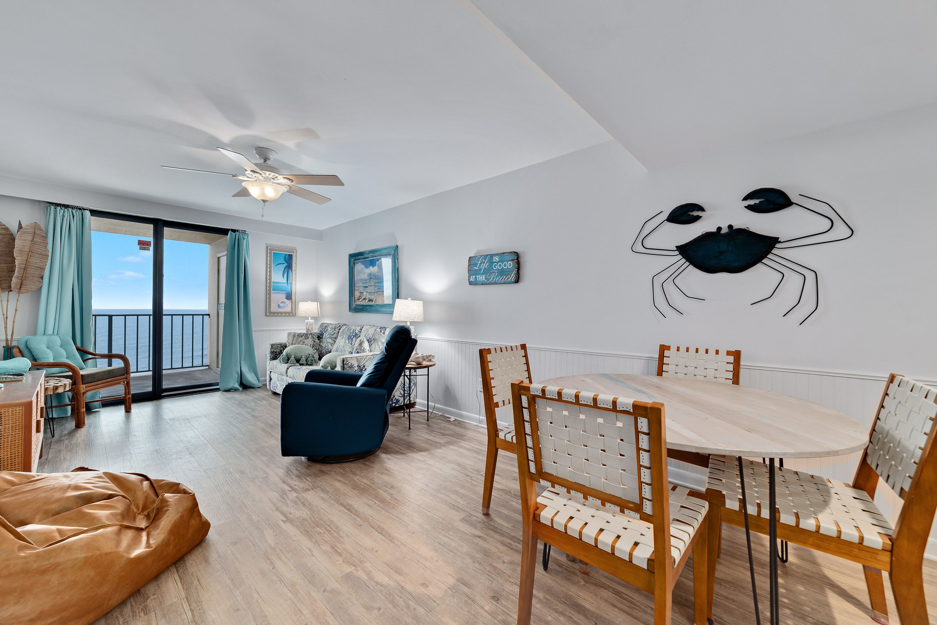 Een ruime woonkamer met een eethoek, een plafondventilator en een groot raam met uitzicht op de oceaan.