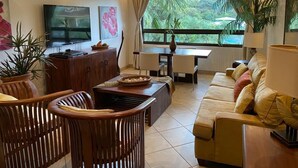 Sala de estar con televisor, muebles de madera, un sofá y un ventanal con vistas a zonas verdes.