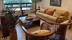 Una sala de estar con sofá, sillas, una mesa de centro y un ventanal con vista a la vegetación.
