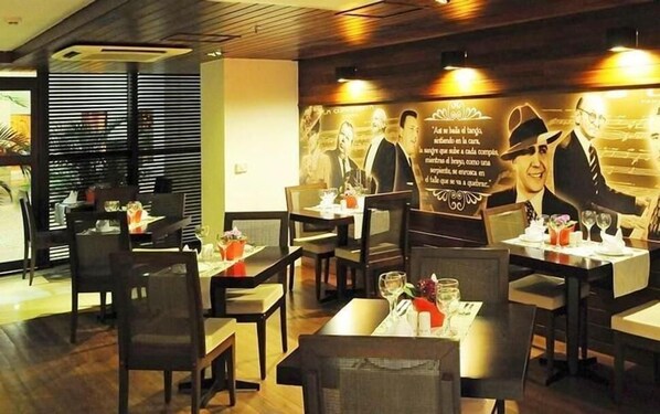 Interior de restaurante com mesas preparadas para refeições, apresentando um mural com texto e imagens na parede.