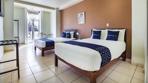 A hotel room with two beds, a ceiling fan, a large window with curtains, a framed picture on the wall, and a small table with a chair. - Capital O Plaza Galindo (San Juan de los Lagos)