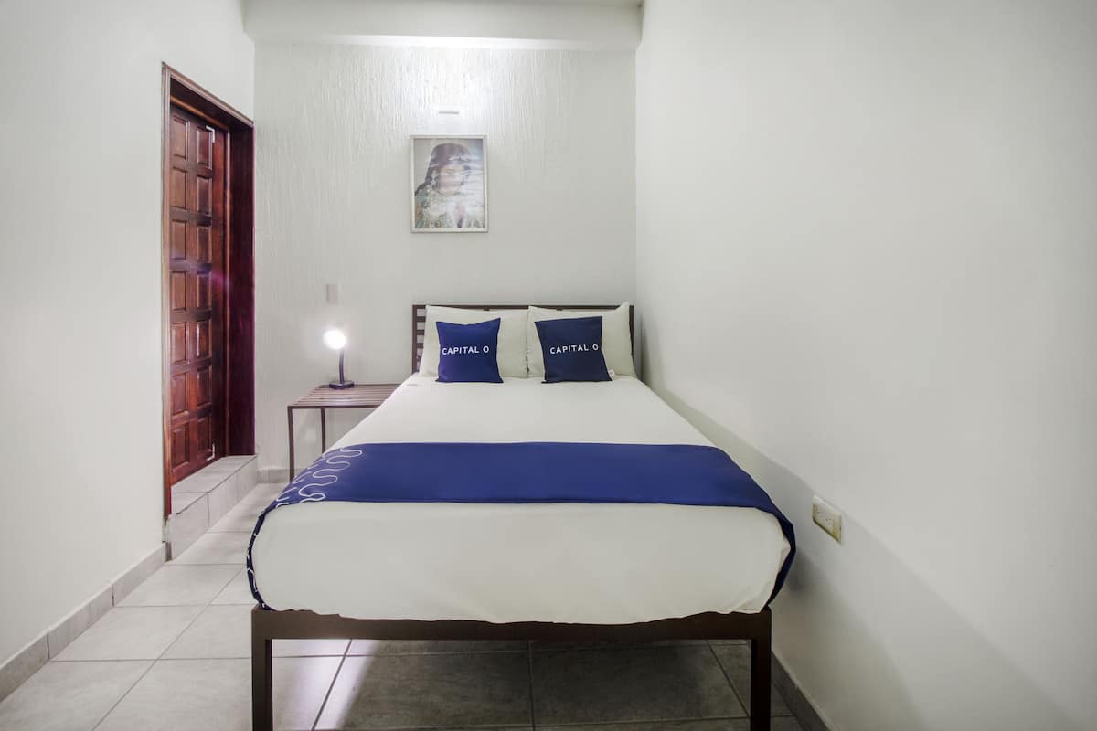 A bedroom with a bed, a nightstand, a wall-mounted lamp, and a door.
