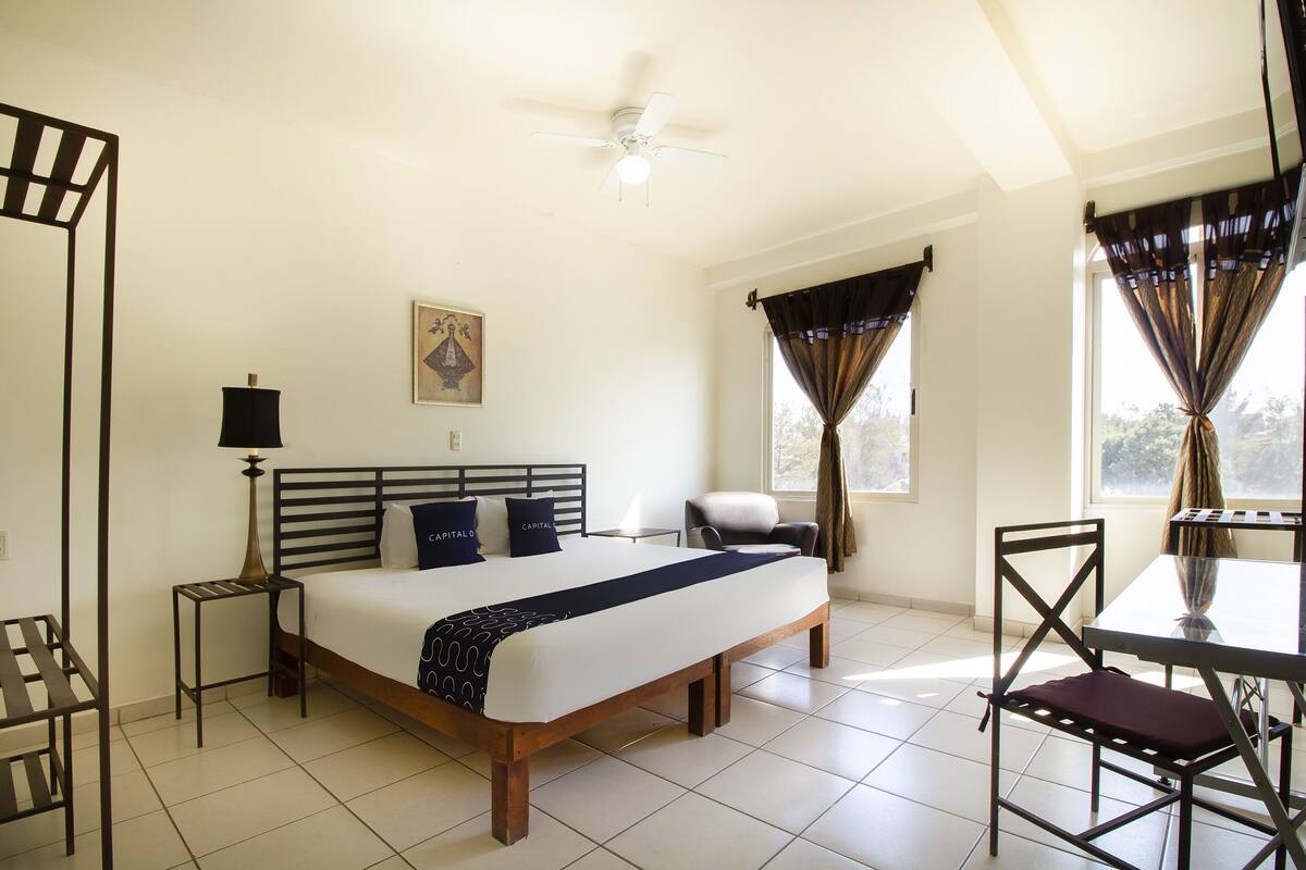 A bedroom with a bed, bedside tables, a chair, a table, and a ceiling fan.