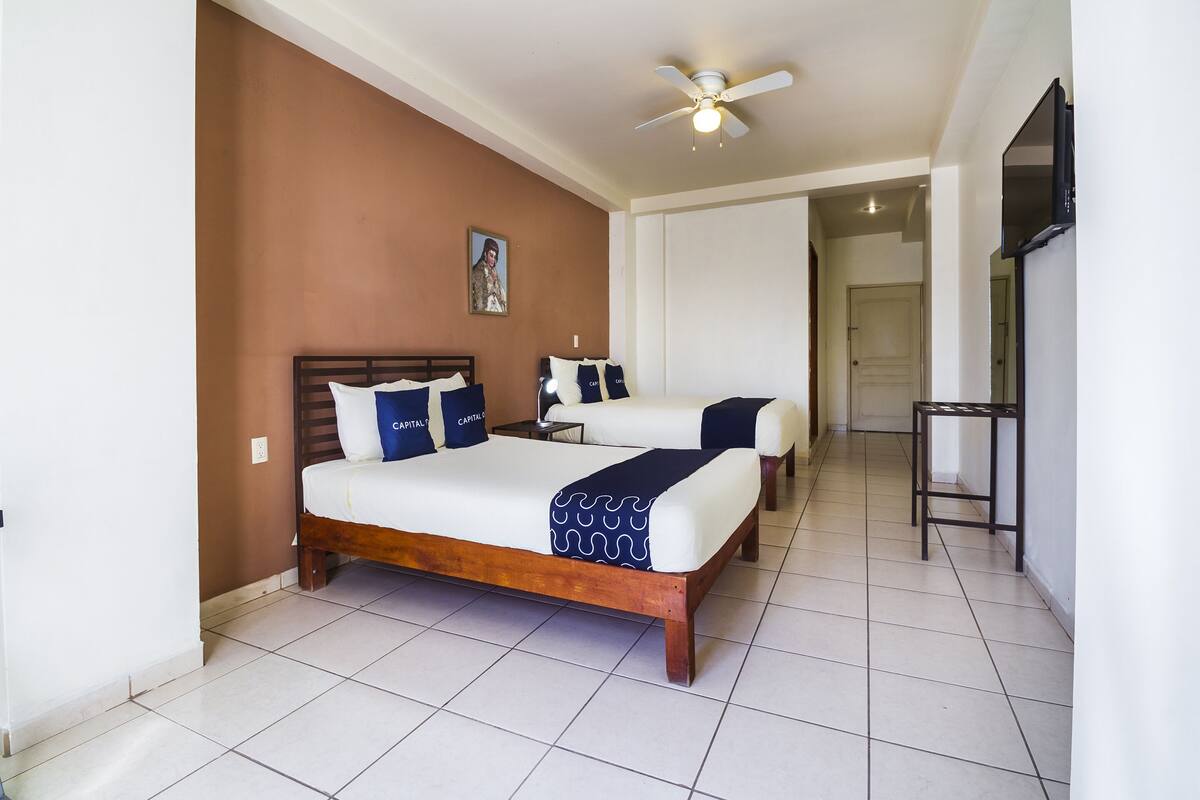 A hotel room with two beds, a ceiling fan, and a television on the wall.